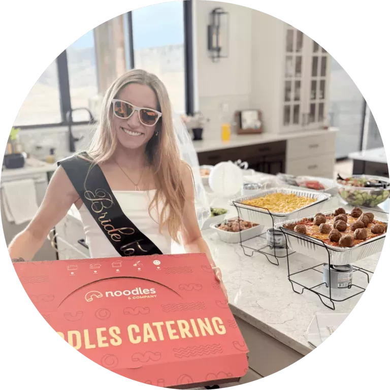 Bride holding a Noodles Catering box in front of a Noodles Catering spread.