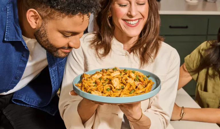 Man smelling a plate of Cajun Shrimp Fettuccine a woman is holding.