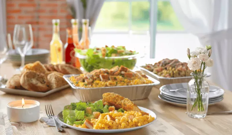 Noodles Catering Spread on a wood table next to an open window with white curtains, flower vase on table.