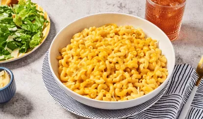 Creamy Cheddar Mac &amp; Cheese in a bowl next to a salad, striped napkin, and glass of water